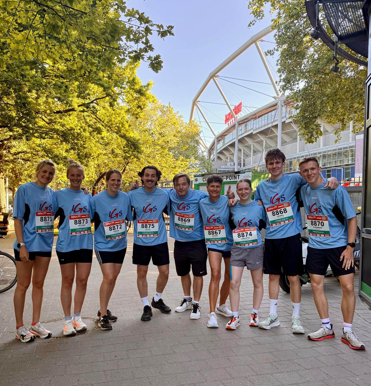 Eine Gruppe von Läuferinnen und Läufern der IGS Langenhagen steht nach dem Lauf fröhlich lächelnd nebeneinander vor der Fußballarena in Hannover.