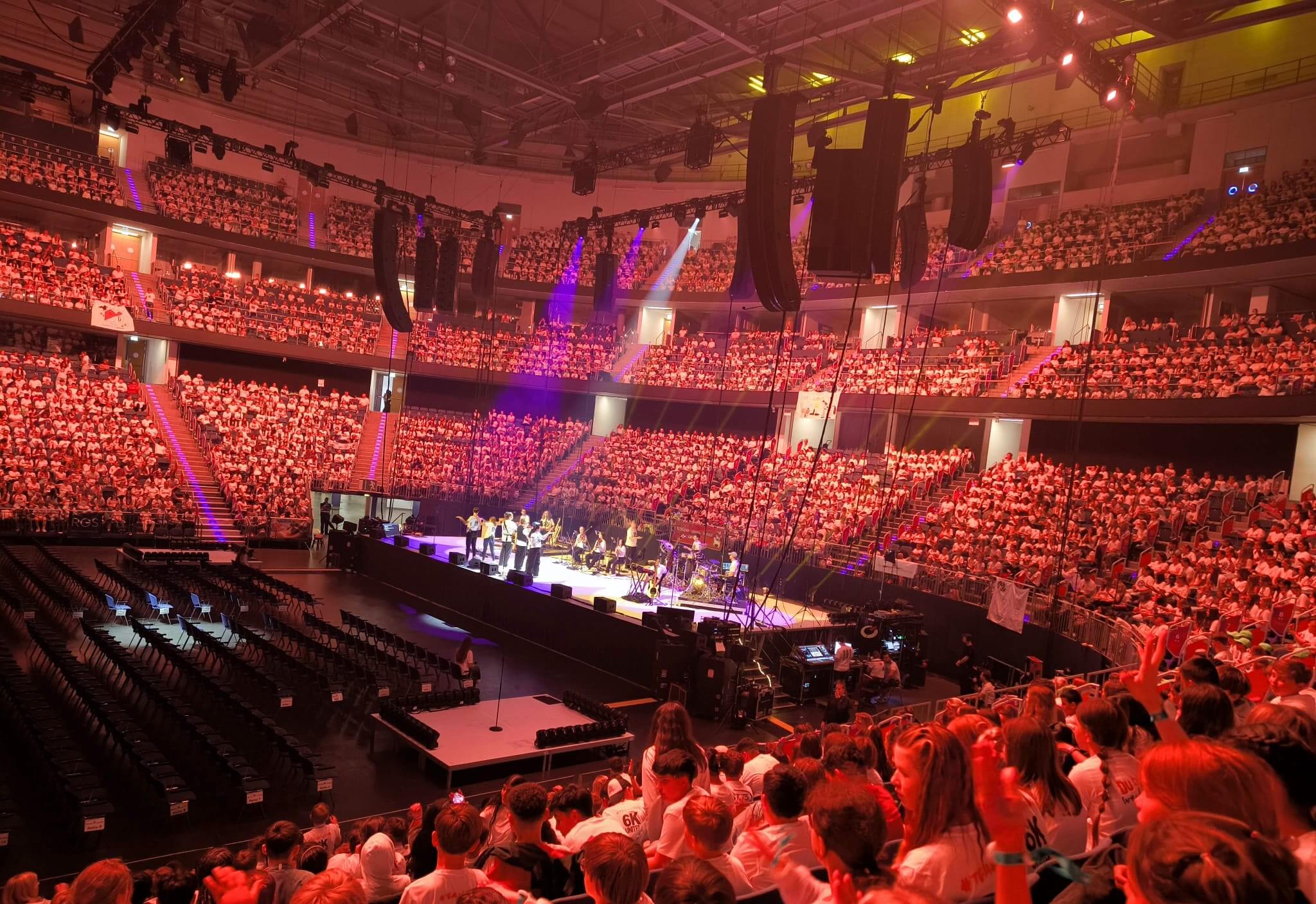 Eine weitwinklige Aufnahme der großen Bühne beim 6K UNITED-Konzert in der ZAG Arena in Hannover. Vor und neben der Bühne stehen tausende Kinder, auf den Rängen sitzen zahlreiche Zuschauer.